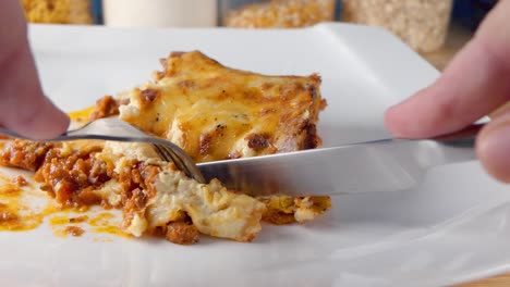 Close-up-Slider-Aufnahme-In-Zeitlupe,-Wie-Man-Mit-Messer-Und-Gabel-Eine-Köstliche-Portion-Lasagne-Auf-Einem-Weißen-Teller-Isst