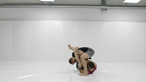 two male wrestlers in a white room work out throwing mats. take a grapple and throw through yourself.