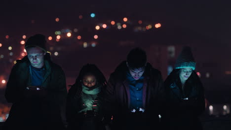 group of friends relaxing on rooftop at night using smartphone technology browsing social media chatting online enjoying weekend gathering