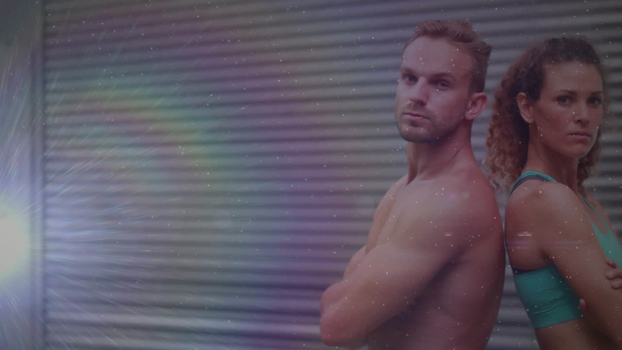 Duo posing back-to-back, studio light creating flare, shifting, giving thumbs-up promoting fitness