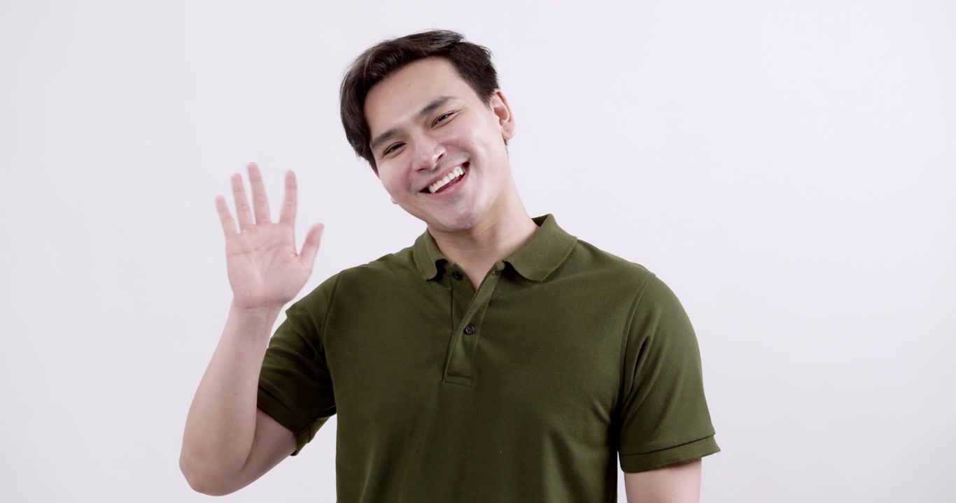 A cheerful young man waves hello showcasing a friendly demeanor in a simple studio setting radiating positivity.