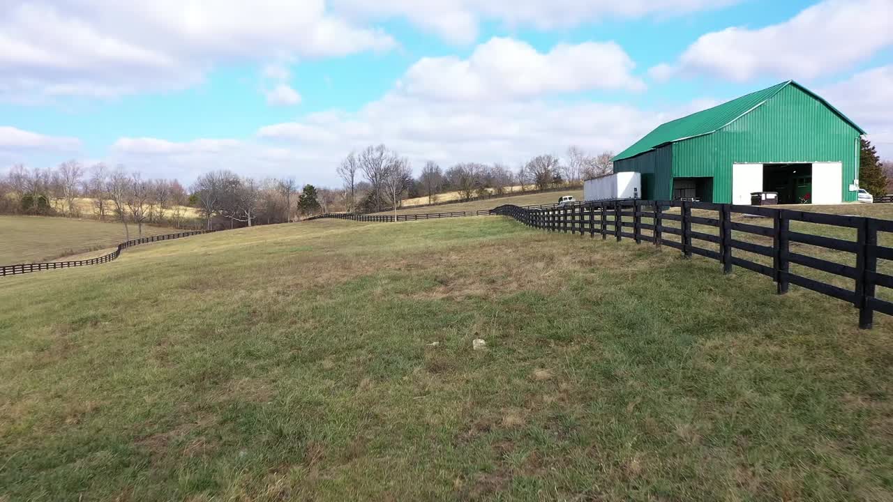 antena moviéndose hacia abajo por una fila de vallas en una granja de caballos en kentucky con un gran granero verde en el estado de bluegrass derecho