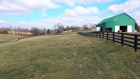 Antena-Moviéndose-Hacia-Abajo-Por-Una-Fila-De-Vallas-En-Una-Granja-De-Caballos-En-Kentucky-Con-Un-Gran-Granero-Verde-En-El-Estado-De-Bluegrass-Derecho