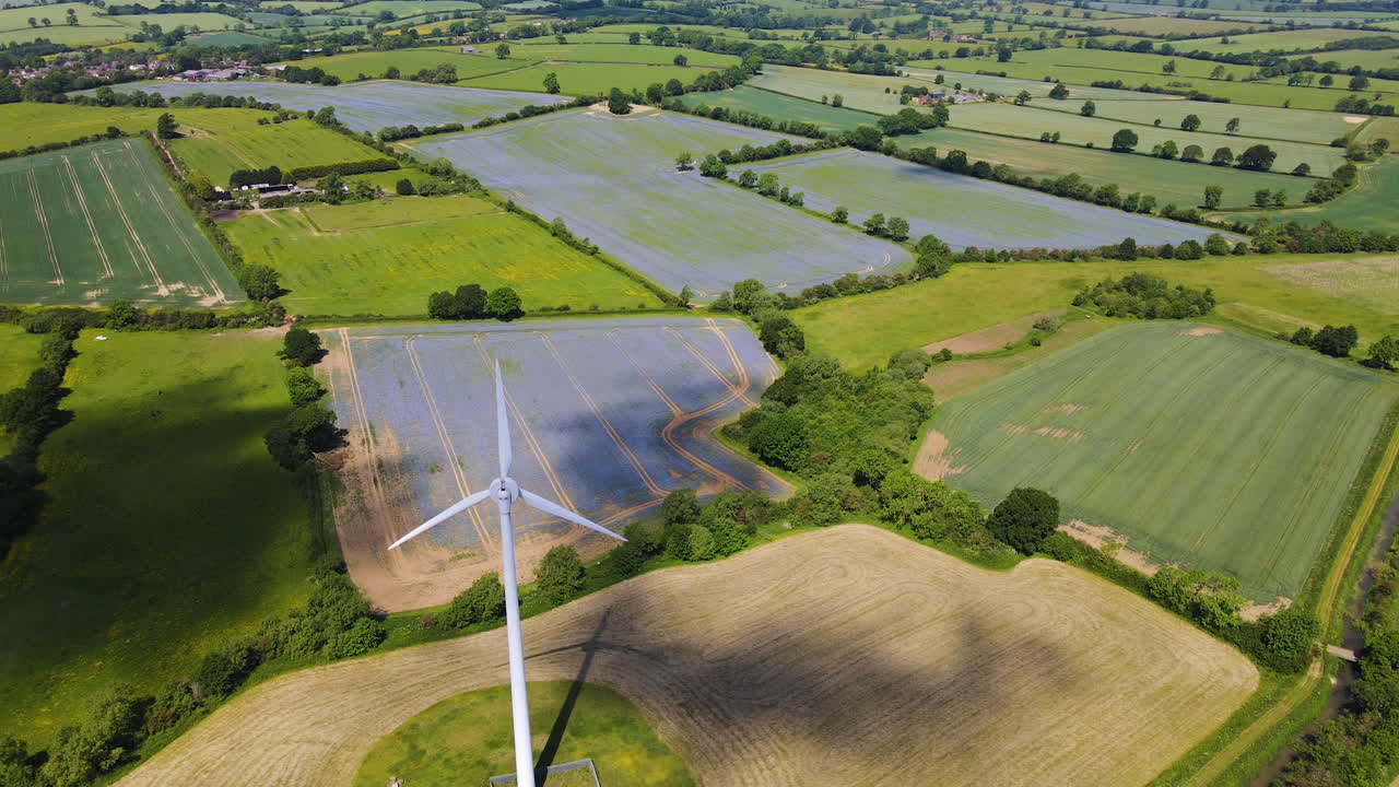 Drone footage of wind turbine generating clean renewable energy amongst farm fields and countryside in Northamptonshire, England