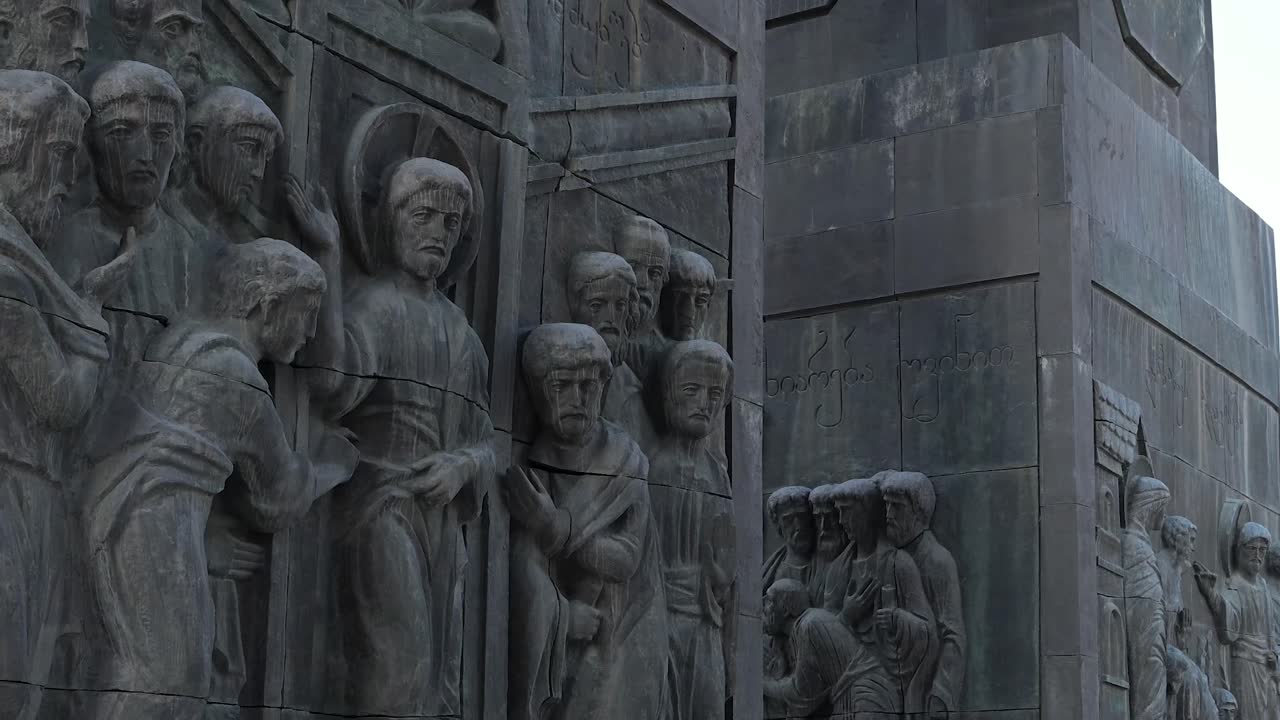 Visitors walk among the monumental sculptures at Chronicle of Georgia in Tbilisi highlighting human scale against dramatic carved pillars