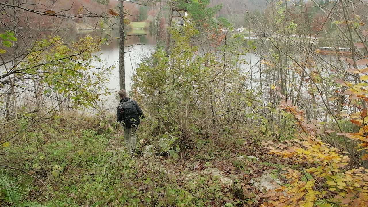 una persona caminando por una pequeña colina hacia el borde del lago con una mochila rodeada de hermosa naturaleza