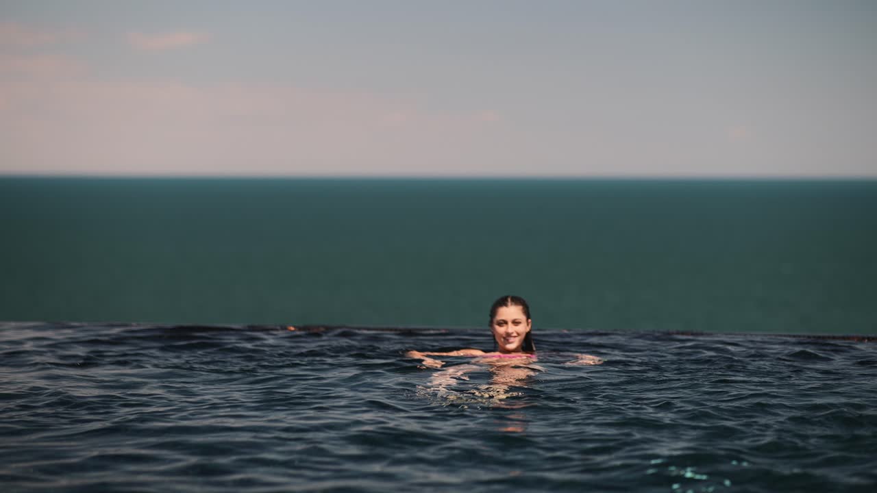 mujer nadando en la piscina infinita con vista al océano