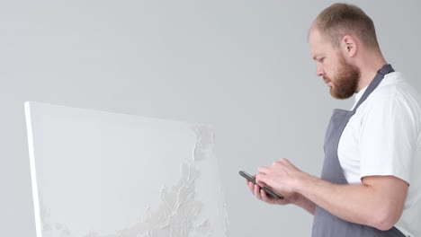 a young artist sits at home on a stool in front of a canvas and works with inspiration paints a