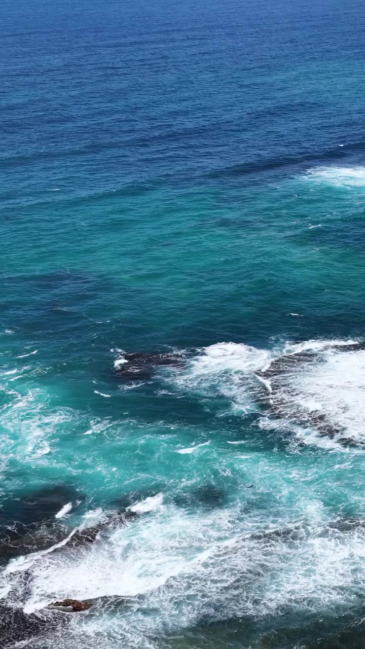 Il filmato con drone ad alta angolazione cattura onde turchesi che si infrangono su rocce scure lungo la costa.