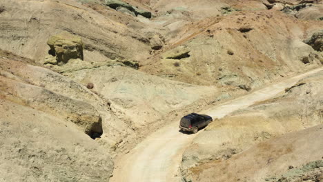 dark black suv 4x4 drives down a dry dirt road in the mojave desert on a sunny day