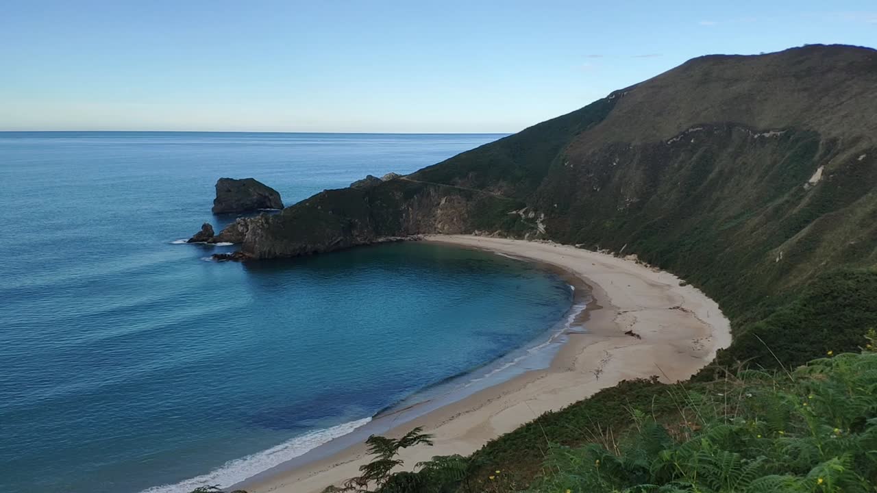 Secluded bay beach in Asturias with turquoise sea and green cliffs all around
