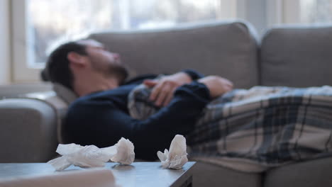 man-sick-lying-down-on-sofa-and-blowing-his-nose-with-tissue