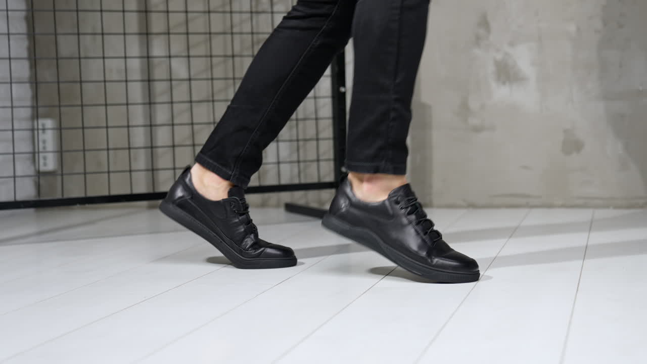 Unrecognized man in black jeans and leather sneakers showing moonwalk. Stylish male footwear demonstration in studio.