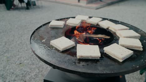 grilling bread slices on a wood-fired outdoor circular grill, rustic cooking setup