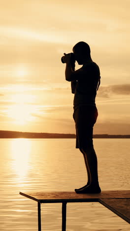photographer taking picture of landscape during sunset. silhouette of people swimming in the river at sunset. vertical video