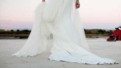 Tiro-De-ángulo-Bajo-De-La-Novia-Con-Vestido-Blanco-Saliendo-De-Un-Coche-Clásico-Al-Atardecer