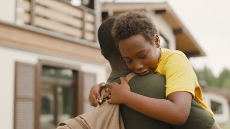 military father holding and embracing his sad son outside home