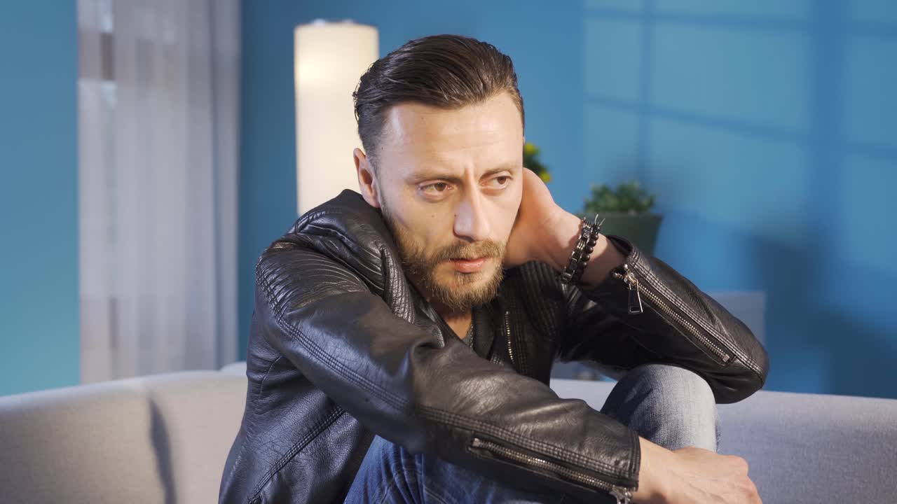 Portrait of worried handsome man with personal problems sitting on sofa at home feeling stressed and hopeless.
