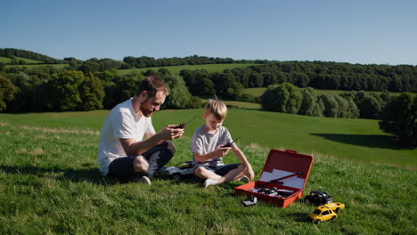 father and son playing with rc cars on a grassy hill