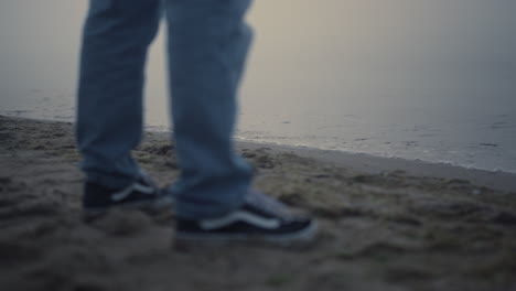 guy legs sneakers standing on sea beach. unknown man feet wearing casual shoes