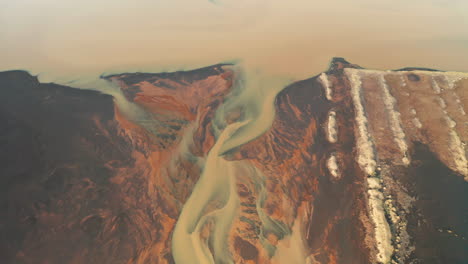 drone flying above yellow riverbed on black sand beach in south iceland - aerial, pullback shot