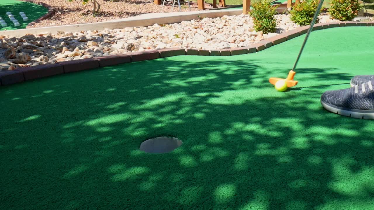 Putting a yellow golf ball in mini golf with an orange putter on green astroturf
