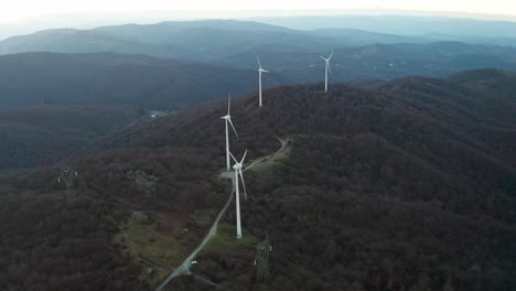 wind turbines dominate the crest of forested hills in a fading light, an aerial view of sustainable energy in the wilderness