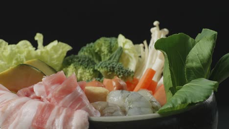 close up of a pot of shabu ingredients spinning around on the black background