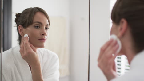 middle-aged caucasian woman applies skincare in a home bathroom