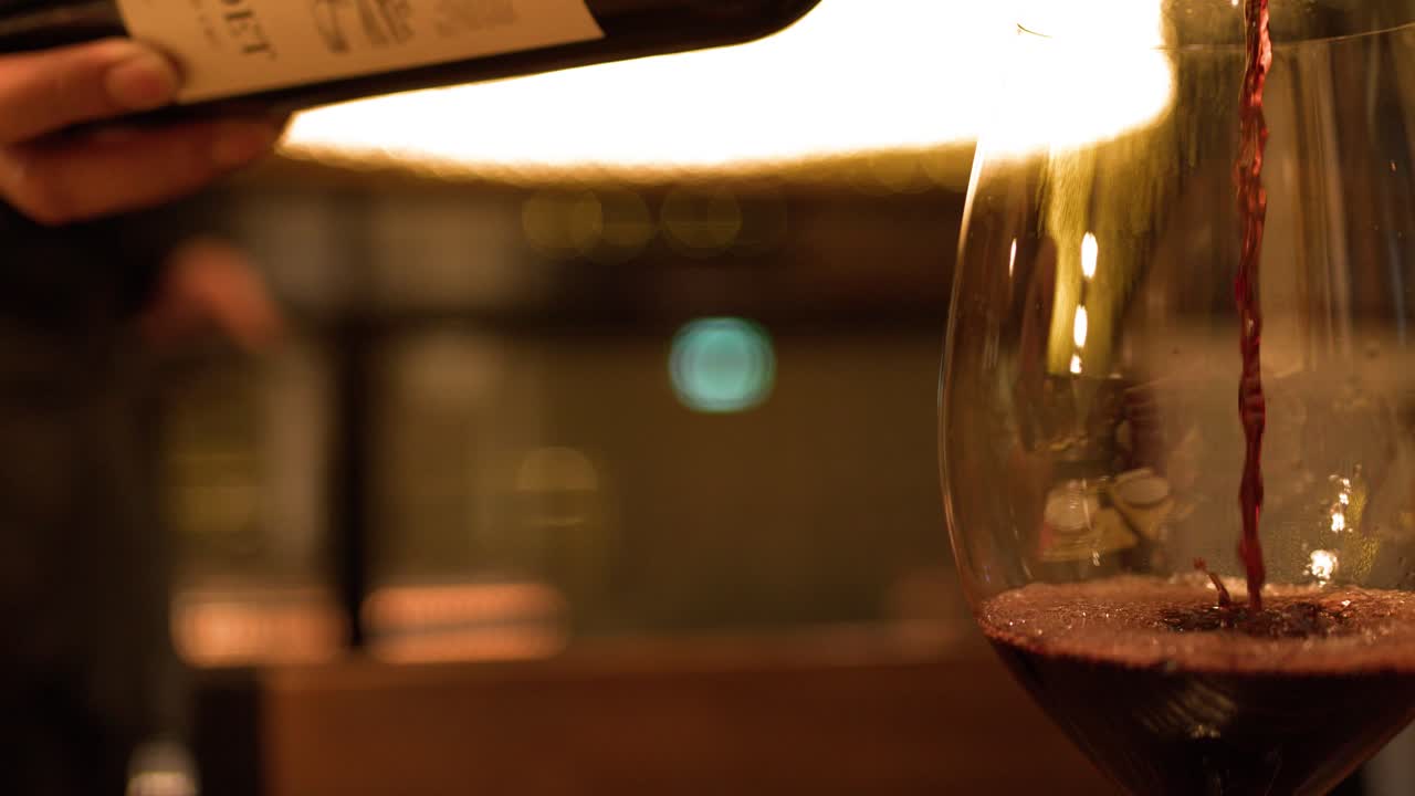 Un primo piano mostra del vino rosso versato in un bicchiere sotto una calda ed elegante illuminazione da ristorante