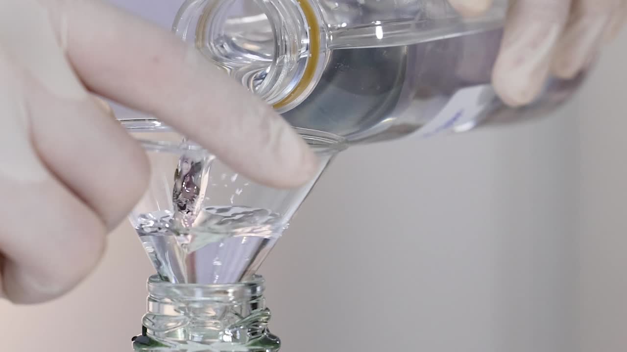 Scientist Pouring Liquid Through Funnel into Bottle