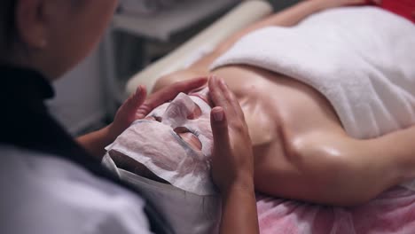 close up view of a professional cosmetologist hands making face massage to the young woman with mask on her face and neck