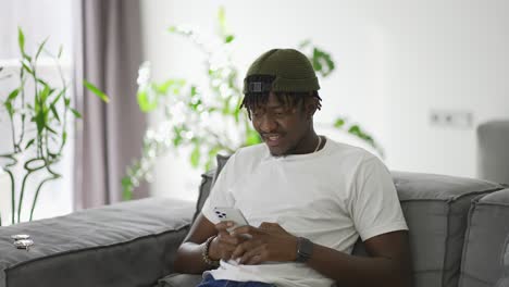 African-American-man-using-smartphone-while-resting-on-a-sofa-in-living-room