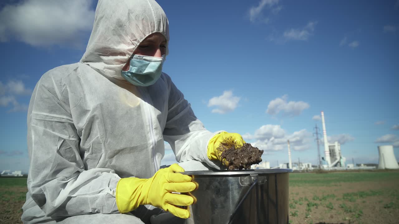 científico en traje protector comprobando la contaminación del aceite en el suelo, fondo industrial, vista de gran angular al aire libre