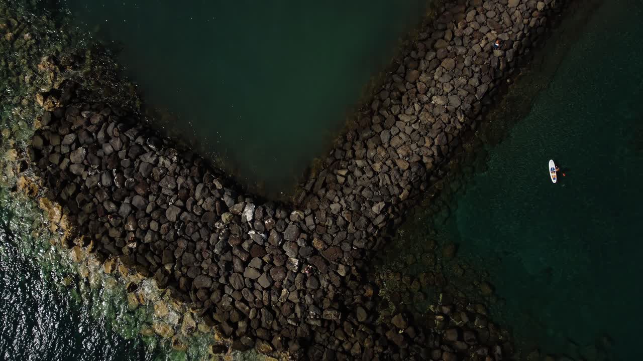 Grande formazione rocciosa in riva al mare con surfista, ripresa da drone a Tenerife, Spagna, Los Cristianos.