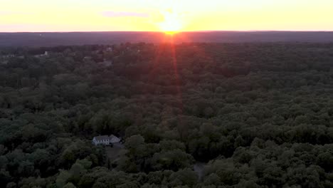 reverse aerial flight over forested area of the northeastern usa tilts down from intense sunset to the forest.