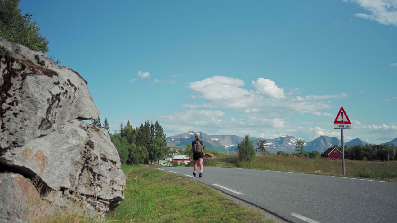 Hiker With Backpack Walking At Cemented Road Under The Summer Weather In Norway. - wide shot