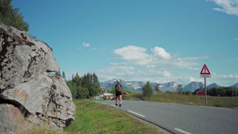 hiker with backpack walking at cemented road under the summer weather in norway. - wide shot