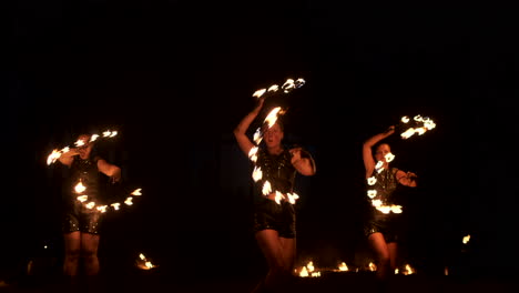 Slow-motion:-Professional-fire-performance-three-women-in-dripping-clothes-dance-and-spin-with-flaming-torches-and-a-man-with-flamethrowers-in-the-background.