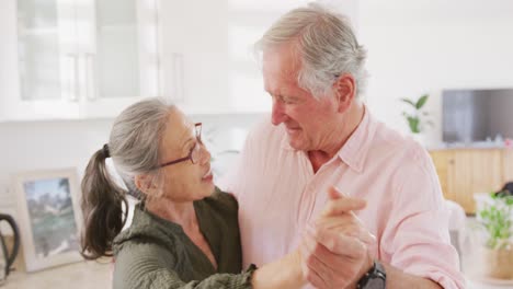 feliz pareja de ancianos diversos tomados de la mano y bailando en la cocina