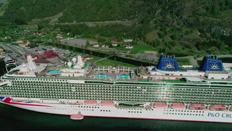 Luftaufnahme-Des-Schönen-Dorfes-Flam-In-Norwegen-Mit-Blick-Auf-Das-Grüne,-Besiedelte-Wohngebiet-Mit-Farbenfrohen-Gebäuden-Und-Einem-Großen-Passagierschiff-Mit-Mehreren-Schwimmbädern-Für-Touristen