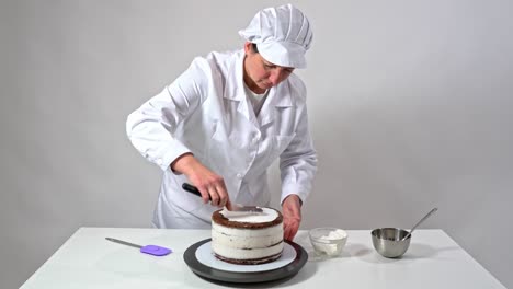 fotografía frontal de un panadero usando una espátula de helado para tocar cuidadosamente los lados del pastel cubierto de crema.