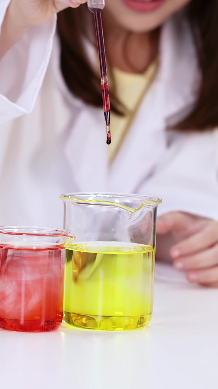Primo piano di uno studente che usa una pipetta per far cadere del liquido in becher durante la lezione di scienze