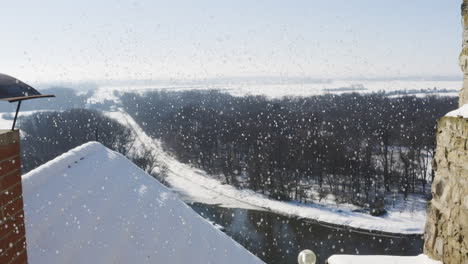 Chimenea-De-Ladrillo-En-Un-Techo-Sobre-Un-Río-Y-Bosques,-Nieve-Que-Cae,-Invierno