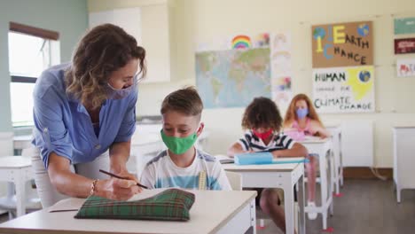 maestra que usa una máscara para la cara enseñando a un niño en clase en la escuela