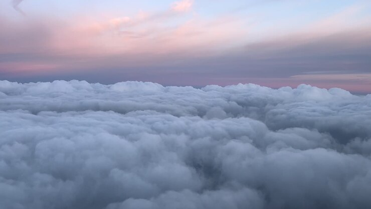 POV flying over a layer of clouds with a pastel color sky at sunset, shot from a jet cockpit