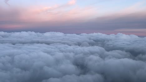 POV-flying-over-a-layer-of-clouds-with-a-pastel-color-sky-at-sunset,-shot-from-a-jet-cockpit