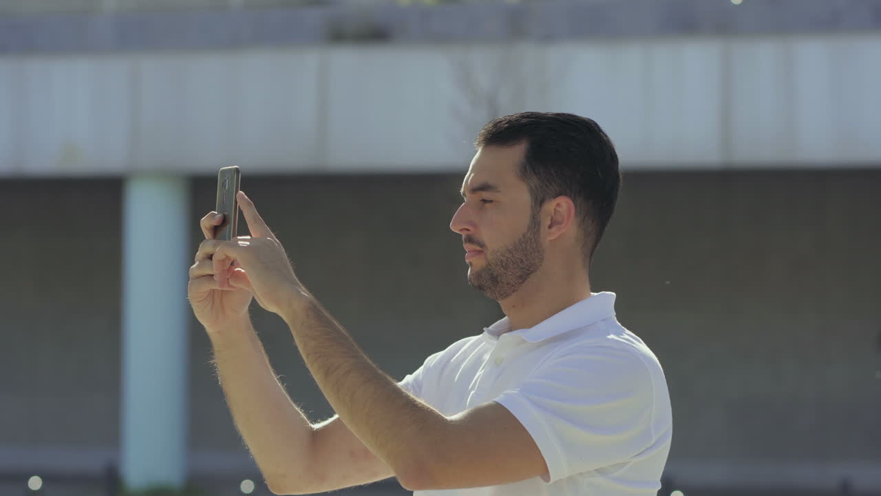 Jovem barbudo concentrado gravando vídeo com o smartphone