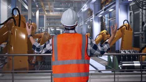 back view of a male engineer with safety helmet spreading arms while standing with industrial robotic arms working