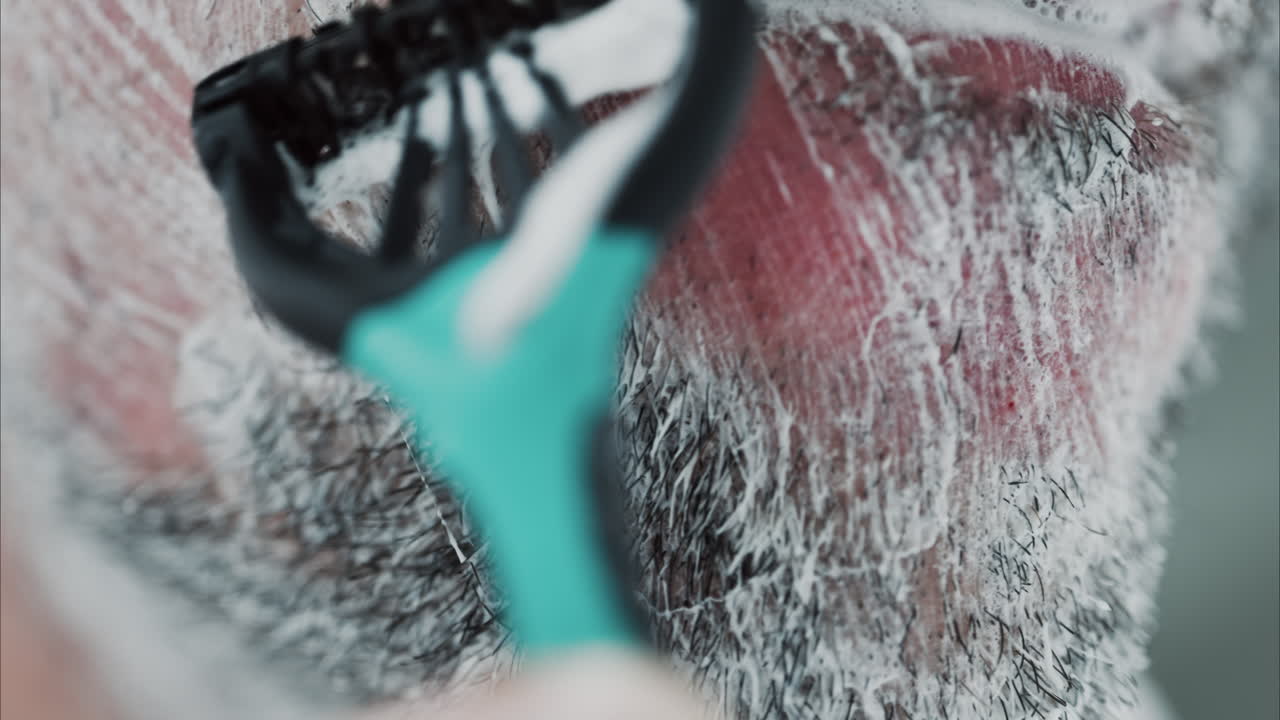 Close up of a man shaving his beard with a razor